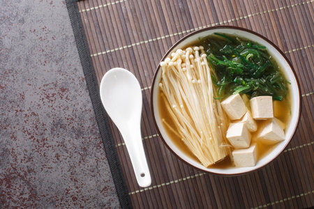 Rich miso soup with enoki mushrooms, wakame seaweed and tofu, vegetarian, vegan Asian food close-up in a bowl on the table. Horizontal top view from aboveの写真素材