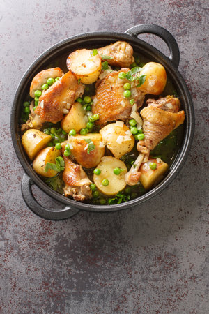 Delicious pieces of chicken cooked with potatoes and green peas close-up in a frying pan on the table. Vertical top view from aboveの写真素材
