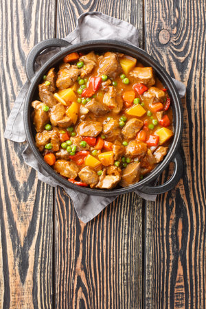 Veal stew with vegetables potatoes, carrots, green peas, onions and spices close-up in a frying pan on a wooden table. Vertical top view from aboveの写真素材