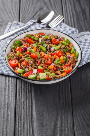 Summer lentil salad with onions, carrots, cucumber, peppers and tomatoes close-up in a plate on a wooden table. Verticalの写真素材