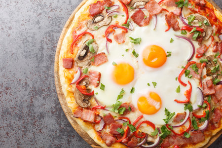 Homemade pizza with bacon, eggs, peppers, mushrooms and red onions close-up on a wooden board on the table. Horizontal top view from aboveの写真素材