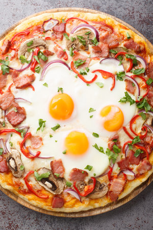 Freshly baked pizza with bacon, eggs, peppers, mushrooms, mozzarella and red onions close-up on a wooden board on the table. Vertical top view from aboveの写真素材