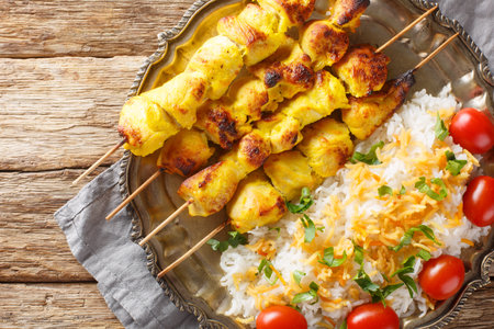 Grilled saffron chicken skewers with rice garnish close-up in a plate on a wooden table. horizontal top view from aboveの写真素材