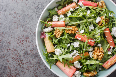 Healthy spring salad with baked rhubarb, arugula, goat cheese and walnuts close-up in a bowl on the table. Horizontal top view from aboveの写真素材