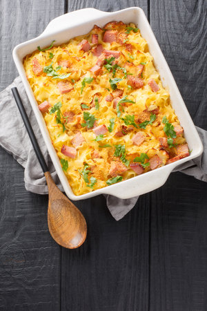 Austrian pasta Fleckerl baked with ham, sour cream egg sauce and breadcrumbs close-up in a baking dish on the table. Vertical top view from aboveの写真素材
