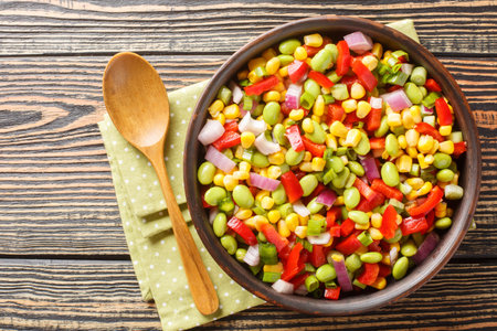 Vitamin salad of summer vegetables with edamame soybeans, bell peppers, corn, tomatoes and onions close-up in a bowl on the table. Horizontal top view from aboveの写真素材