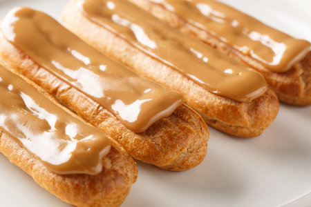 Fresh classic eclairs with cream filling and covered with caramel sauce close-up in a plate on the table. Horizontalの写真素材