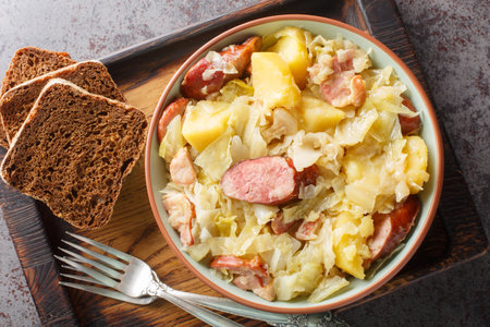 Hunter's cabbage stewed with sausage, potatoes, bacon and onions close-up in a bowl on the table. Horizontal top view from aboveの写真素材