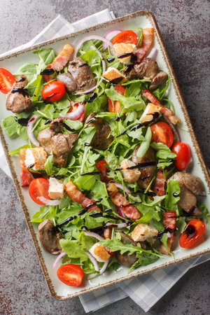 Warm chicken liver salad with bacon, cherry tomatoes, arugula. red onion and croutons close-up on plate on table. Vertical top view from aboveの写真素材