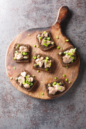 Sandwiches with canned cod liver, green onions and capers close-up on a wooden board on the table. Vertical top view from aboveの写真素材