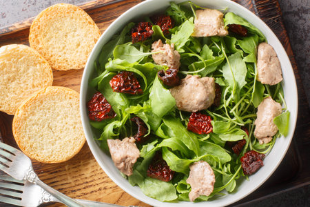 Delicious cod liver salad with arugula and sun-dried tomatoes served with toast close-up in a bowl on the table. Horizontal top view from aboveの写真素材