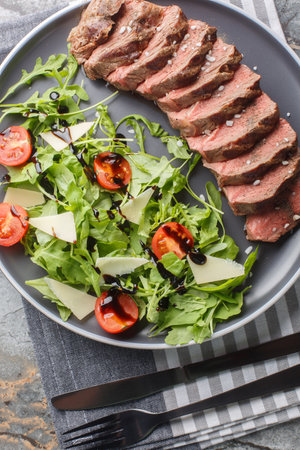 Beef tagliata with arugula, parmesan and cherry tomatoes is a delicious main course made with beef entrecote close-up on a plate on the table. Vertical top view from aboveの写真素材