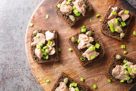 Tasty sandwiches with code liver, capers and green onion close-up on a wooden board on the table. Horizontal top view from aboveの写真素材