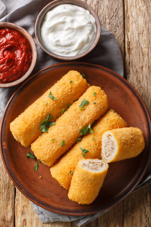Polish Krokiety Croquettes are pancakes rolled with stuffing, breaded and fried in a pan closeup on the plate on the wooden table. Vertical top view from aboveの写真素材