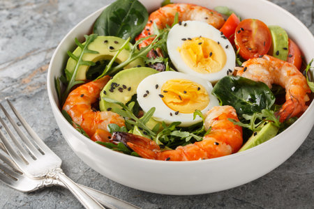 Balanced breakfast salad with shrimp, avocado, arugula, spinach, tomatoes and boiled eggs close-up on a bowl on the table. horizontalの写真素材