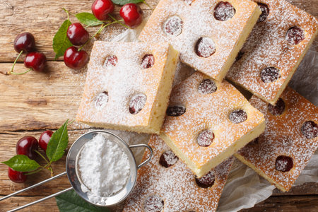 Czech bublanina cherry cake sprinkled with powdered sugar closeup on the parchment on the wooden table. Horizontal top view from aboveの写真素材