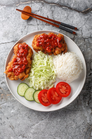 Ayam geprek an Indonesian fried chicken with sambal sauce served with white rice, cucumber, tomato and cabbage closeup on the plate on the table. Vertical top view from aboveの写真素材