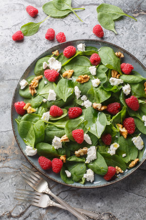 Summer salad of spinach, raspberries, feta and walnuts close-up in a plate on the table. Vertical top view from aboveの写真素材