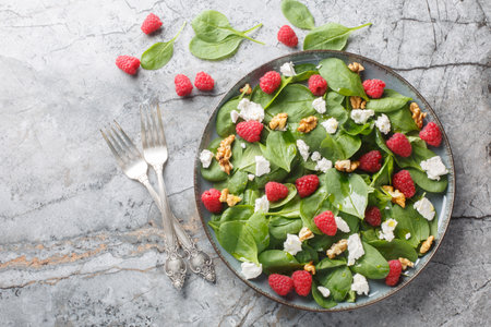 Baby spinach with raspberries, feta and walnuts close-up in a plate on the table. Horizontal top view from aboveの写真素材