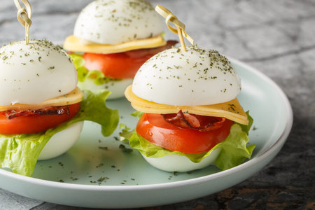 Snack on skewers of hard-boiled eggs with cheese, bacon, tomato and lettuce close-up in a plate on...