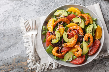 Shrimp salad with citrus fruits such as orange and grapefruit, as well as avocado, red onion and leafy greens close-up in a plate on the table. Horizontal top view from aboveの写真素材