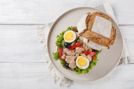 French Pan Bagnat sandwich with salad nicoise consisting of hard-boiled eggs, tuna, vegetables and seasoned with olive oil close-up on a plate on a wooden table. Horizontal top view from aboveの写真素材