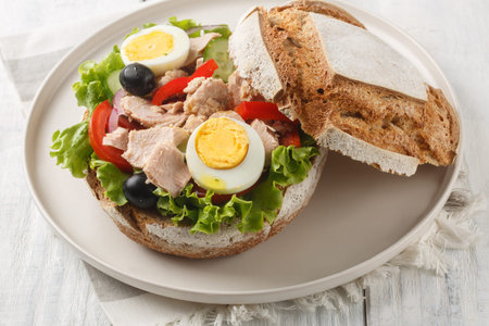 French Pan Bagnat sandwich with salad nicoise consisting of hard-boiled eggs, tuna, vegetables and...