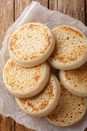 Freshly baked Crumpet is a round pancake made of porous dough close-up on a parchment on a table. Vertical top view from aboveの写真素材