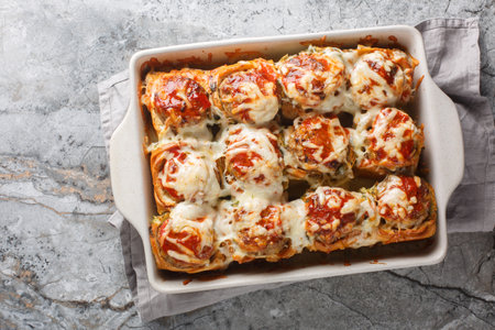 Homemade baked sliders stuffed with meatballs, topped with tomato sauce and grated cheese close-up in a baking dish on a table. horizontal top view from aboveの写真素材