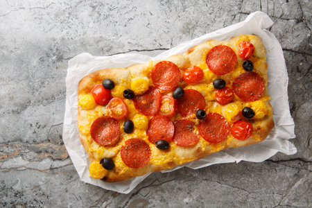Fragrant homemade pinsa romana with tomato mix, peperoni sausage, black olive and cheddar cheese closeup on parchment paper on the table. Horizontal top view from aboveの写真素材
