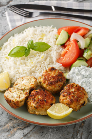 Greek chicken meatballs with feta cheese served with lemon rice and vegetable salad close-up in a plate on the table. verticalの写真素材
