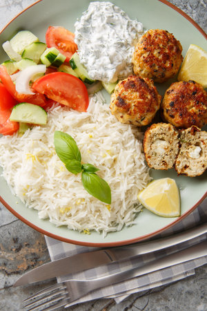 Homemade chicken meatballs with feta cheese, herbs and sun-dried tomatoes served with lemon rice, tzatziki sauce and fresh salad close-up in a plate on the table. vertical top view from aboveの写真素材