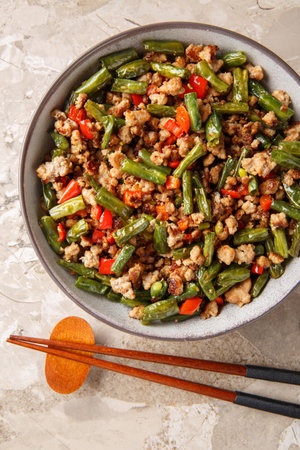 Asian stir-fried green beans with minced pork, bell pepper, garlic and ginger close-up in a bowl on the table. Vertical top view from aboveの写真素材