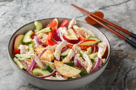 Diet salad with shredded chicken, cucumber, apple, red onion, bell pepper and sesame seeds in Asian style close-up in a bowl on the table. horizontalの写真素材