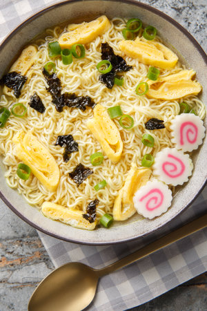 Saimin soup made from egg noodles and a dashi broth with great toppings like nori, omelette, kamaboko and green onions closeup in the plate on the table. Vertical top view from aboveの写真素材