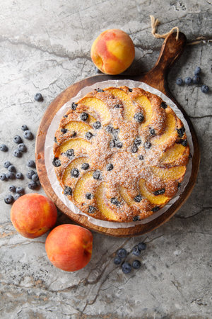 Peach blueberry sponge cake sprinkled with powdered sugar close-up on wooden board on table. Vertical top view from aboveの写真素材