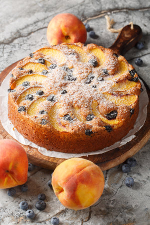 Peach blueberry sponge cake sprinkled with powdered sugar close-up on wooden board on table. Verticalの写真素材