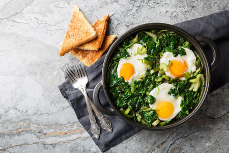 green shakshuka is healthy, one-pan and full of fresh herbs, spinach, and eggs closeup on the pan on...