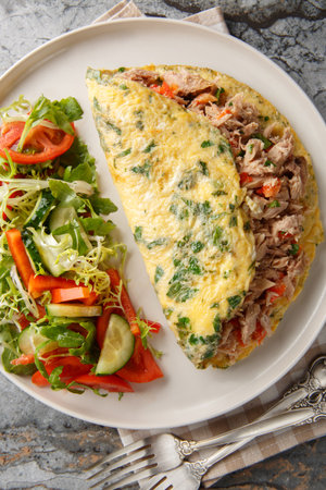 Omelet with canned tuna fish served with fresh vegetables salad closeup on the plate on the table. Vertical top view from aboveの写真素材