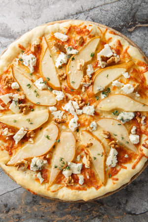 Pear pizza with blue cheese, walnuts, mozzarella and thyme close-up on a wooden board on the table. Vertical top view from aboveの写真素材