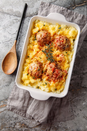Italian Casserole: beef meatballs and mashed potatoes with cheese, tomato sauce, and thyme in a baking dish on the table. Vertical top view from aboveの写真素材