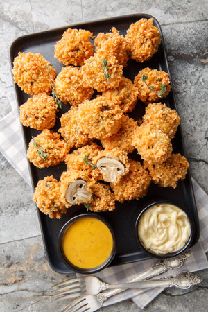 Crispy Fried Mushrooms in breadcrumbs served with sauces close-up in a plate on the table. Vertical...