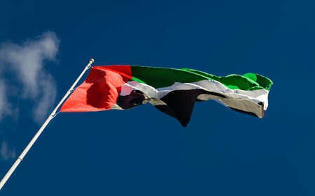 UAE national flag waving in the wind against blue sky background low angle close up. United Arab Emirates symbol.の写真素材