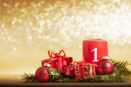 red candle decorated for Christmas with baubles and gifts in front of golden glittering backgroundの写真素材