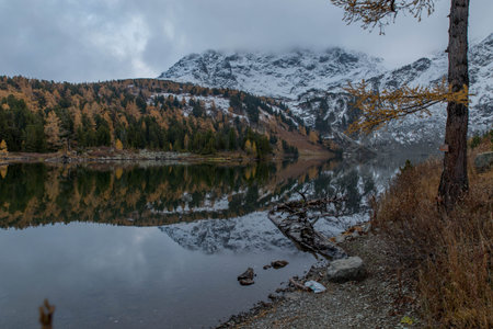 Mirror surface of a crystal clear lake. Colorful autumn forest. A mountain covered with snow. Rocks...