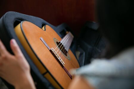 Woman observes and removes a classic brown guitar from a black caseの写真素材