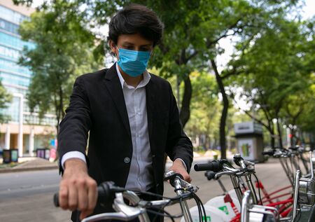 Stock photo of man taking a bicycle in the street. He is wearing a protective mask for the prevention of a virus. Coronavirus conceptの写真素材