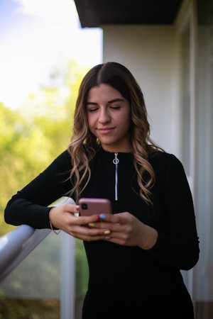 Young woman standing alone outside and sending a text message on her cellphone