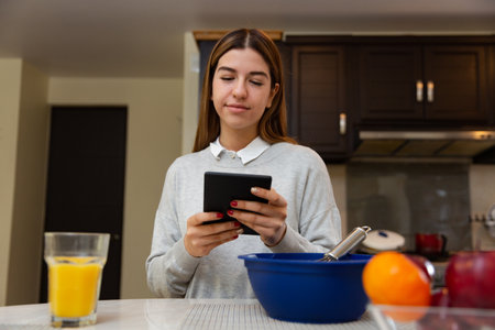 Young woman is learning to cook with her tablet. She is smiling. She is in her kitchen.の写真素材