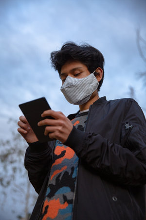 Young latin man with mask is using his tablet in the streetの写真素材